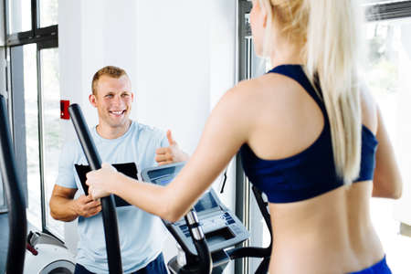 Young woman exercising on an orbitrec with an assissting trainer
