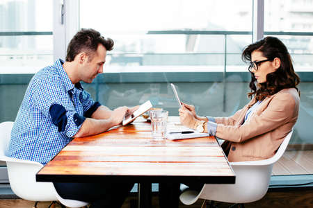Young couple sitting at a table and using their digital tabletsの写真素材