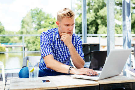 Young man sitting outdoors and browsing the internet on a laptop