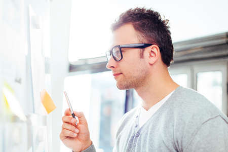 Freelancer looking at his ideas written on paper and stuck to a wallの写真素材