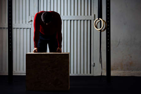 Tired sports man after box jumping exercise leaning on box. Dark picture.の写真素材