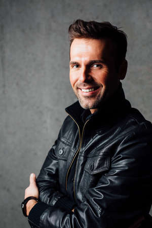Portrait of happy man in leather jacket isolated against concrete wallの写真素材