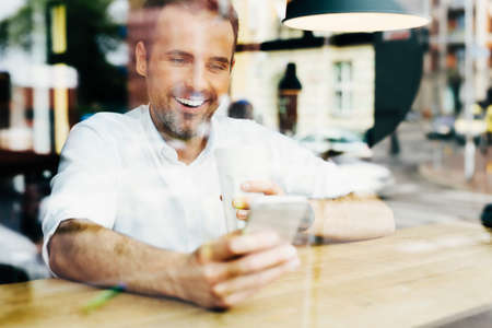 Photo of happy man looking at smartphone in cafe.の写真素材