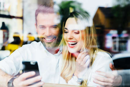 Couple having fun using smartphone at cafe
