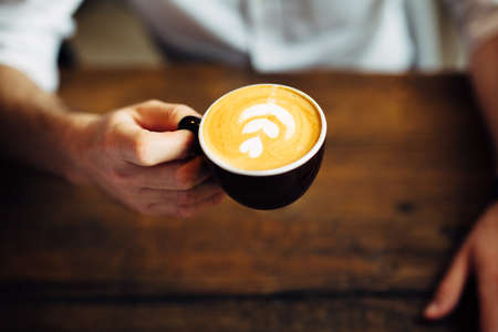 Photo of a man holding coffee cup with flower shape on foamの写真素材