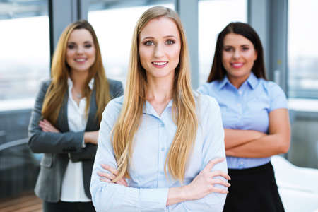 Three female business partners standing in an office and looking at the cameraの写真素材