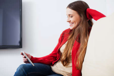 Young happy woman sitting on sofa with digital tablet