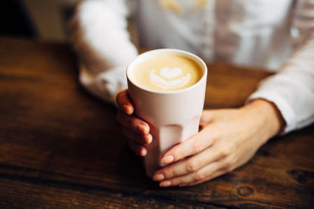 Closeup of woman hands holding coffee with art shapeの写真素材