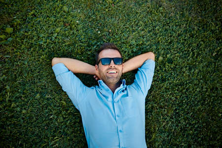 attractive man with sunglasses relaxing on the grass with his hands under the headの写真素材