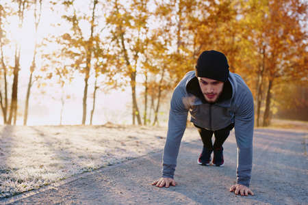 young man doing push ups exercise in park during fallの写真素材