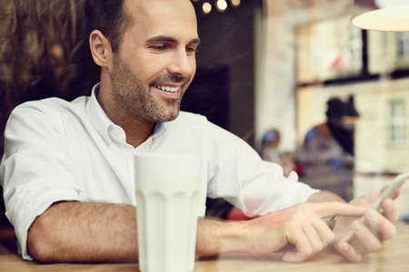 Handsome man in coffee shop using his smartphoneの写真素材
