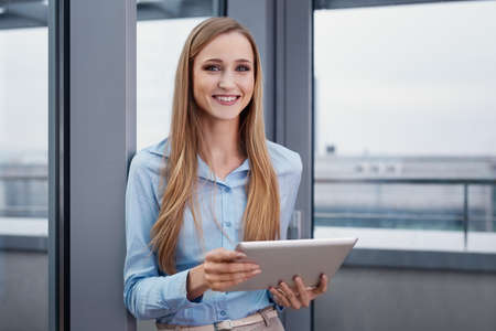 Cheerful woman at office standing with digital tabletの写真素材