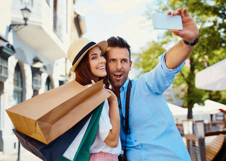 Happy couple taking selfie after shopping in the cityの写真素材