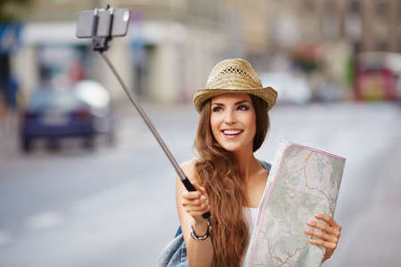 Happy tourist taking selfie with stick, holding map, visiting cityの写真素材