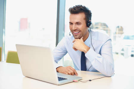 Happy businessman with laptop and headset talking during video conferenceの写真素材