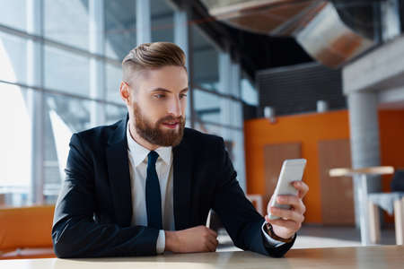 Stylish hipster with suit browsing his smartphone at modern officeの写真素材