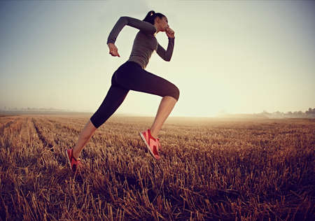 Young woman running fast on field during sunrise