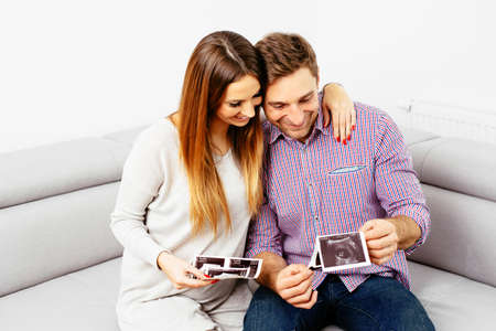 Happy pregnant couple sitting on a sofa and looking at some baby scans