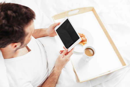 Man sitting in bed and holding a tabletの写真素材