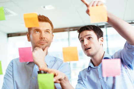 Two businessmen discussing ideas written on sticky notesの写真素材