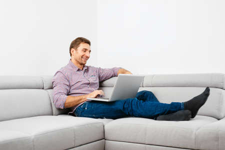 Happy young man sitting on a sofa and using a laptopの写真素材