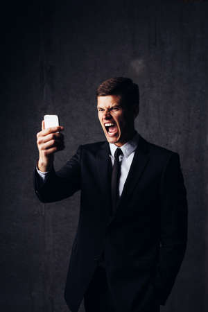 Portrait of a smart businessman looking angrily at his mobileの写真素材