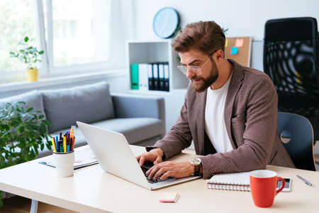Young businessman checking phone while working with laptop in home officeの写真素材