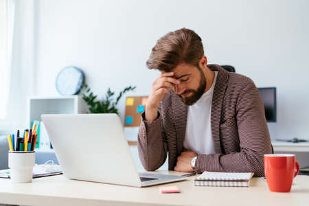 Young businessman checking phone while working with laptop in home officeの写真素材