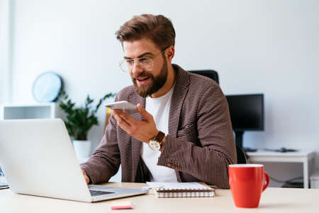 Web designer looking at smartphone while writing notes on whiteboard in modern officeの写真素材