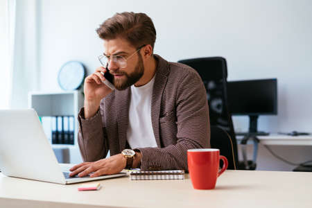 Web designer looking at smartphone while writing notes on whiteboard in modern officeの写真素材