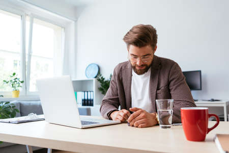 Web designer looking at smartphone while writing notes on whiteboard in modern officeの写真素材