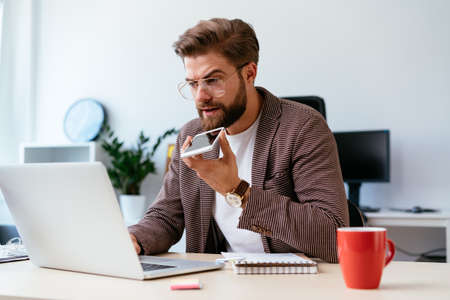 Young startup businessman talking on phone and working on laptop in modern officeの写真素材