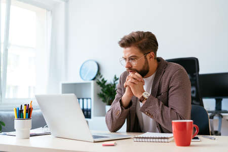 Concentrated businessman looking at laptop and analyzing. Portrait of young startup entrepreneur at workの写真素材
