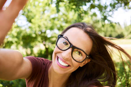Happy young woman taking selfie while relaxing in park during summerの写真素材
