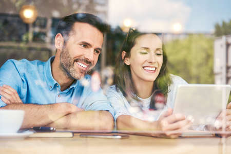 Cheerful couple using tablet while sitting in cafe and having coffeeの写真素材