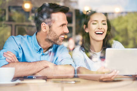 Couple sitting together in cafe looking at tablet and laughingの写真素材