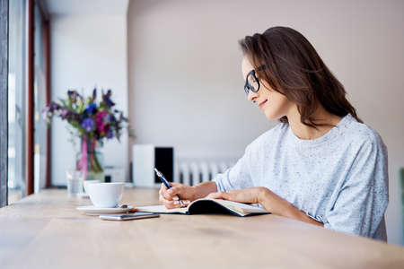 Cheerful young woman using smartphone while having some coffee in cafeの写真素材