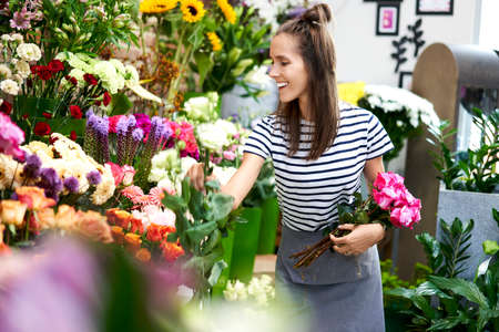 Young florist cutting flower for bouquet at the counter of her shopの写真素材