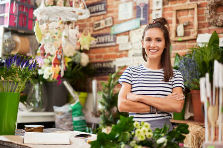 Young florist cutting flower for bouquet at the counter of her shopの写真素材