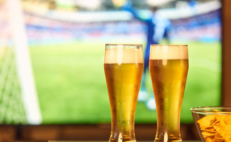 Two glasses of beer in front of TV playing footballの写真素材