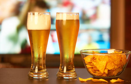 Two glasses of beer in front of TV playing footballの写真素材