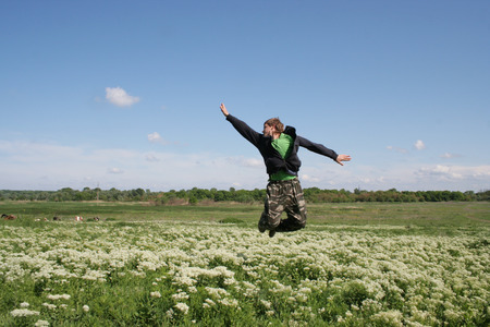 Gracious jump by excited man. Guy flying above flowers field on blue sky backgroundの写真素材