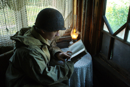 Old fashion picture of patriot soldier in a hamlet reading book with lamp in sepia