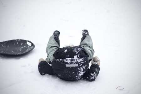 Sledge on snow, boy fell out from sled and up his butt and legs. Kid fools around in winter. Extreme sport funny fall.の写真素材