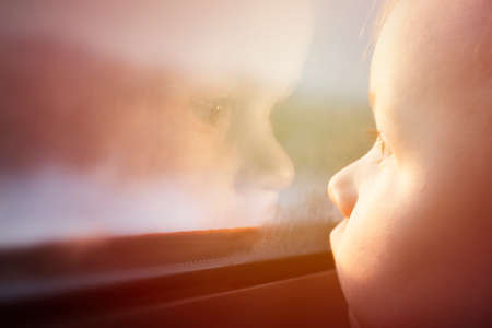 Childhood nostalgia background. Toddler is looking in window with reflectionの写真素材