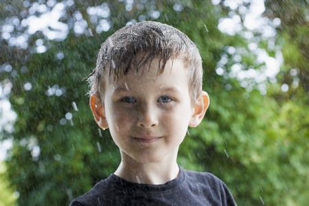 Teenager boy smiling with wet face under rain with green background.  Autumn comes and people surviveの写真素材