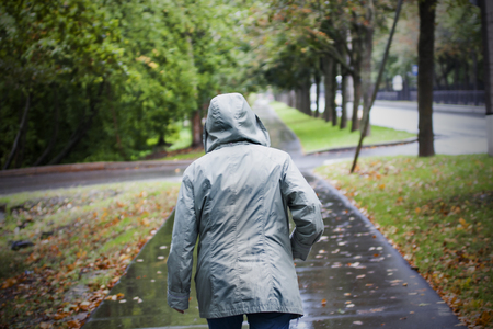 Back of woman in jacket with hood in cold rainy autumn weather. Walking in autumn yellow leaves pathの写真素材