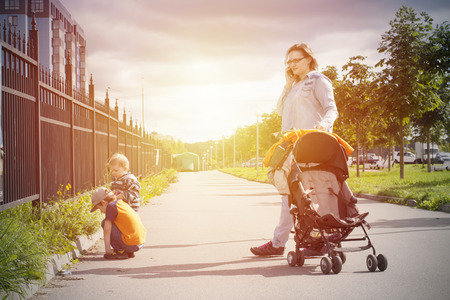 Mom with strolley talk by phone and kids playing in grass. Sunny autumn family walking outdoorの写真素材