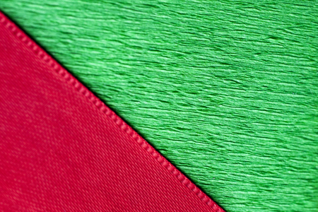Red ribbon and green wrapping paper texture close up. Macro photo of christmas gift boxの写真素材
