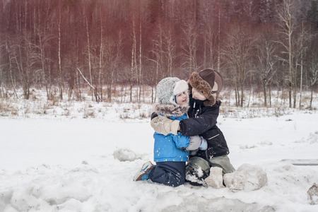 Two happy toddler boys embrace during the play. Kid's friendship in winter snowy forestの写真素材